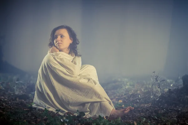 Donna avvolta in un lenzuolo in una oscura foresta nebbiosa — Foto Stock