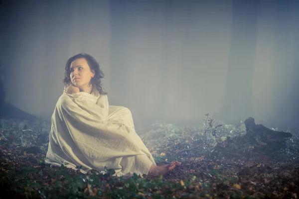 Donna randagio avvolta in un lenzuolo bianco in una foresta nebbiosa — Foto Stock