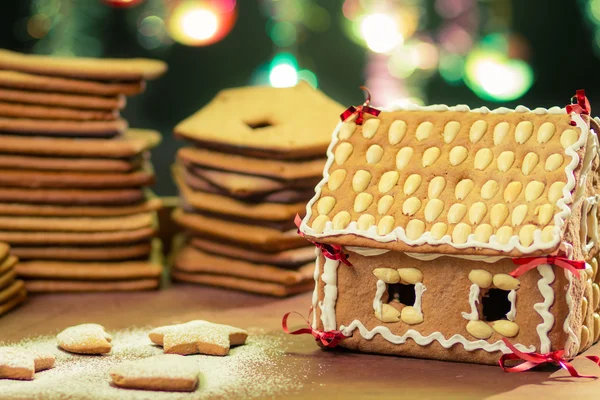 Hausgemachtes Lebkuchenhäuschen gegen einen grünen Weihnachtsbaum — Stockfoto