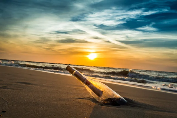 Mensagem com carta dentro da garrafa em uma praia ao pôr do sol — Fotografia de Stock