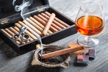 Aroma floating up from cigar and cognac in glass clipart