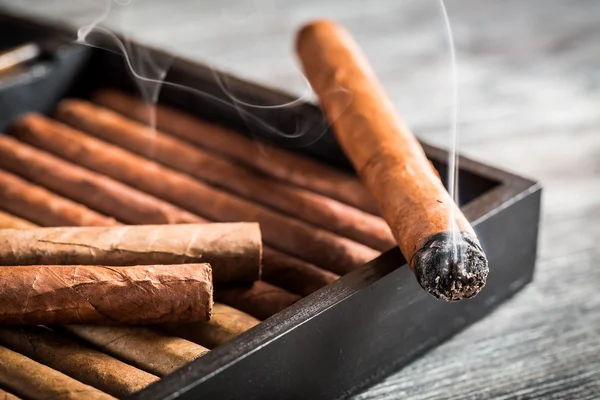 Burning cigar with smoke on old humidor — Stock Photo, Image