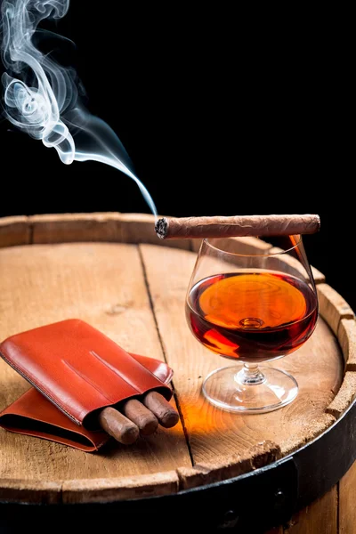 Cigar and cognac on black background with old barrel — Stock Photo, Image