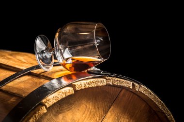 Glass of cognac on the old wooden barrel clipart