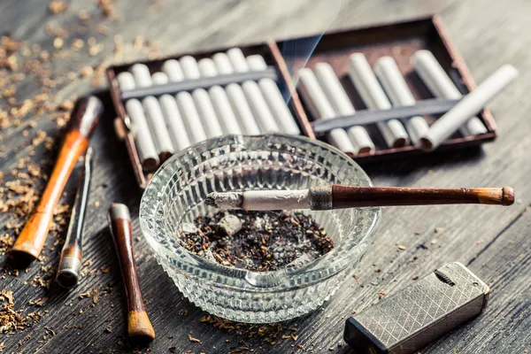 Glass ashtray with thin wooden pipes, cigarettes and lighter aro — Stock Photo, Image