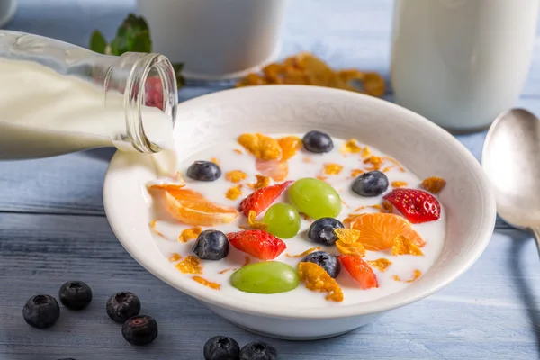 Pouring milk on cornflakes with fruits — Stock Photo, Image