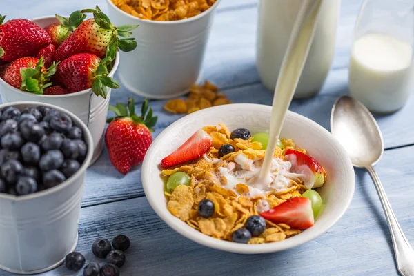 Pouring milk into cornflakes with fruits — Stock Photo, Image