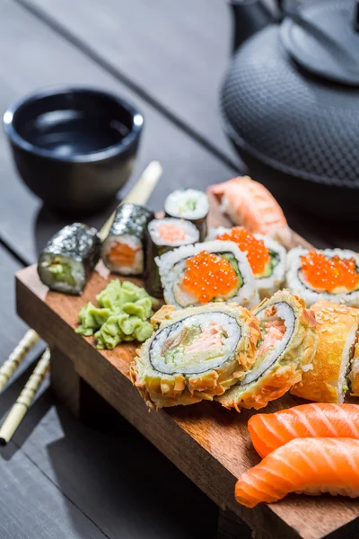 Fresh sushi on wooden board served with tea — Stock Photo, Image