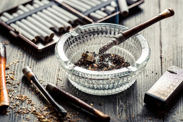 Тонкая трубка в стеклянной пепельнице с сигаретами и зажигалкой — стоковое фото
