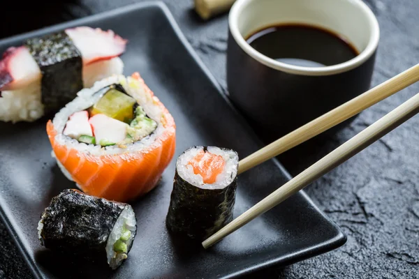 Sushi på svart keramik äts med pinnar — Stockfoto