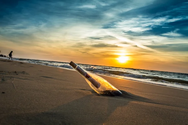 Mensagem com carta dentro da garrafa em uma praia ao pôr do sol — Fotografia de Stock