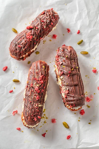 Sweet and chocolate eclairs with strawberries and pistachios. Eclairs with chocolate as perfect snack.