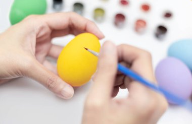 Sarı yumurtaları boyamak için fırça tutan kadın eller. El işi konsepti. Mutlu Paskalyalar. Dekoratif konsept.