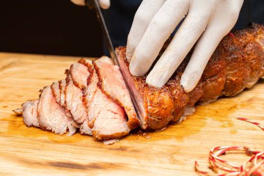 Closed up of chefs hand slicing tender smoked and grilled beef on wooden board. Beef sliced. Western traditional food. 