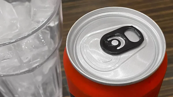 Closed up of Aluminum red soda can with a glass of ice cubes.