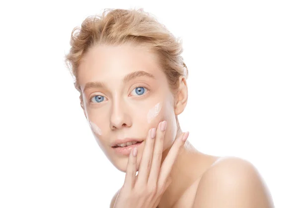 Mulher loira bonita nova com pele clara aplicando creme facial com os dedos, isolada no branco — Fotografia de Stock