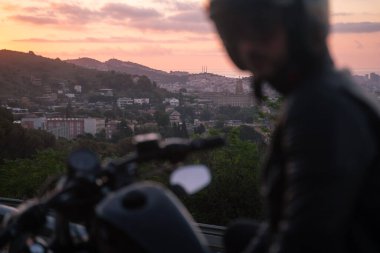 Motosikletlinin gün batımında güzel şehir manzaralı motosikletinin seçici odak noktası.