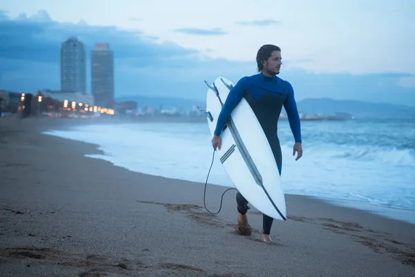 Joven surfista sosteniendo tabla de surf y caminando por la costa, listo para surfear Imágenes de stock libres de derechos