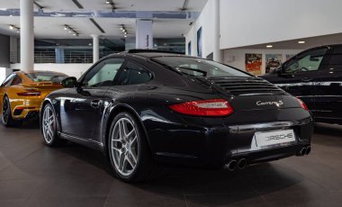 Bir galerinin içinde siyah bir Porsche Carrera S resmi..