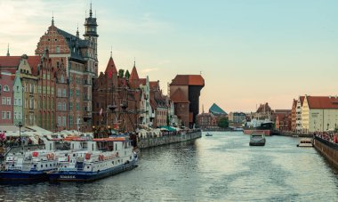 A picture of some Gdansk landmarks next to the river Motlawa, such as the Crane, the St. Mary's Gate and the Black Pearl ship, at sunset.