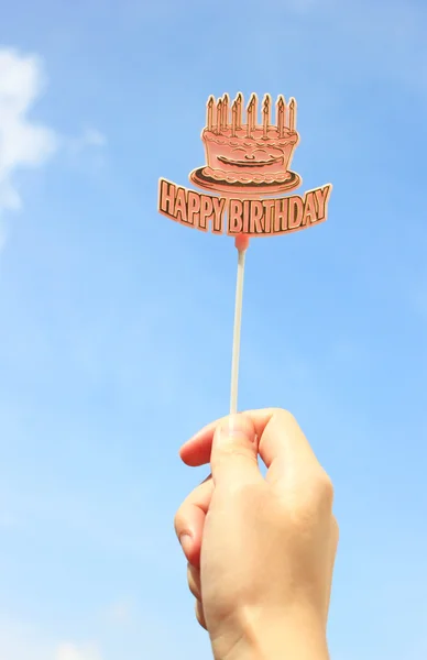 Mão segurando etiqueta de aniversário feliz com céu azul — Fotografia de Stock