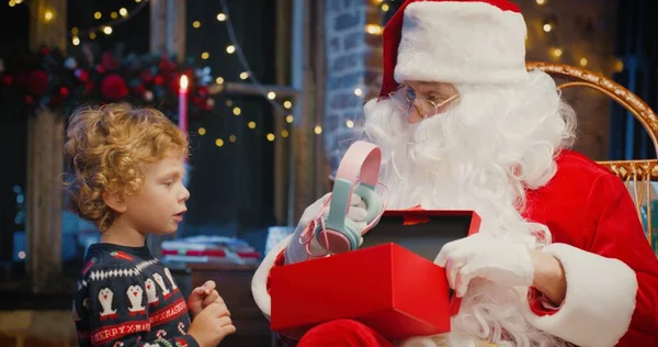 Santa Claus y el pequeño chico caucásico de pie cerca y esperando un regalo mágico de Navidad cerca del árbol de Navidad en la acogedora sala de estar en invierno —  Fotos de Stock