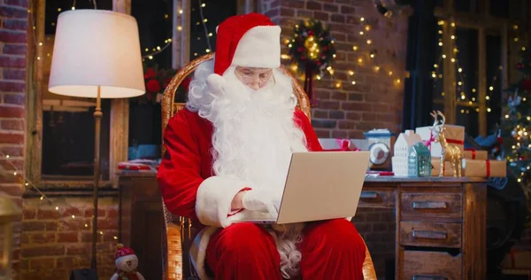 Sluiten van gelukkige senior man in kerstman kostuum typen op de laptop terwijl thuis zitten. Vakantieconcept — Stockfoto