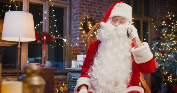 Close up of happy senior man in Santa Clause traje conversando no smartphone com alguém enquanto está sentado em casa. Conceito de feriados — Fotografia de Stock