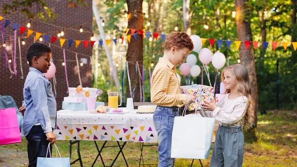 Its for you. Friends giving presents to the birthday girl. Birthday party of small girl outdoors in garden in summer. Celebration concept