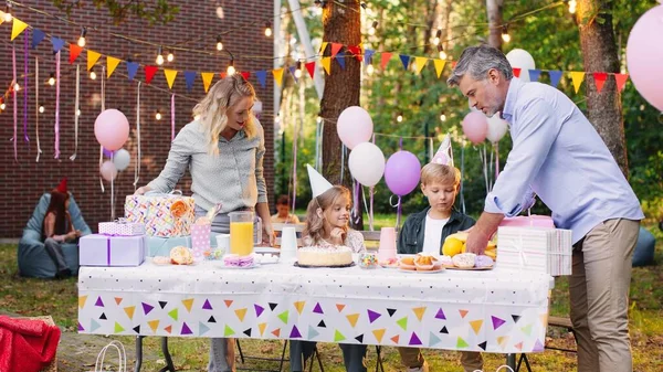 Pais caucasianos alegres servindo mesa para a festa de aniversário de seu filho. Eles filha sentada nas proximidades e esperando a festa — Fotografia de Stock