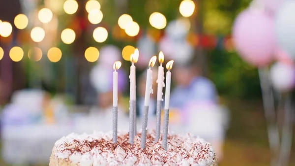 Feche o bolo de aniversário com velas soprando e as pessoas na mesa no jardim ao fundo. Conceito de partido — Fotografia de Stock