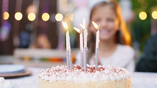 Zamknij tort urodzinowy z dmuchającymi świeczkami i ludzi przy stole w ogrodzie w tle. Koncepcja partii — Zdjęcie stockowe