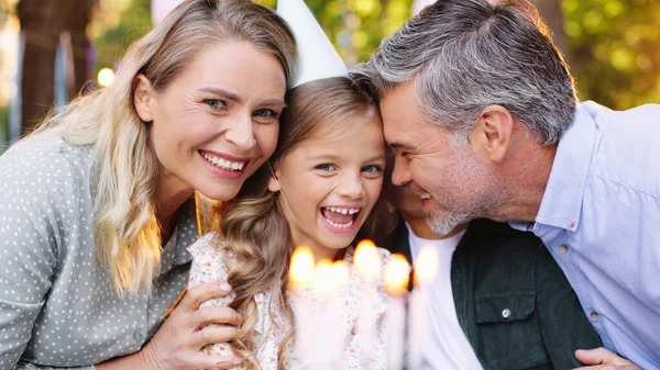 Jonge familie geniet van verjaardagstaart. Portret van een gelukkig meisje dat aan tafel zit met haar ouders en broer terwijl ze zich klaarmaakt om kaarsen te blazen. Gelukkige verjaardag en kindertijd concept — Stockfoto