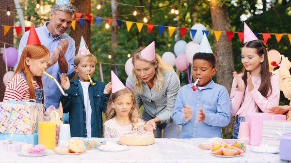 Donna caucasica che porta una grande torta e la mette su un piatto di bambini durante la festa di compleanno in giardino — Foto Stock