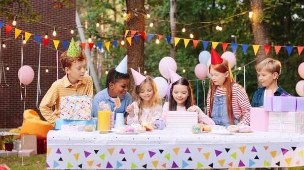 Születésnapi lány. Gyerekek sapkában a születésnapjukat ünneplik a természetben. Asztal finom ételekkel és ajándékokkal. A barátok gratulálnak a legjobb barátjuknak. Boldog gyerekek a születésnapi party koncepciójában — Stock Fotó