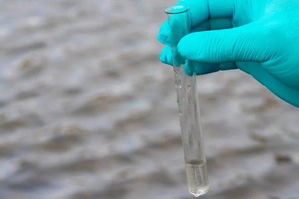 A water sample from the river. Hand in glove collects water in a test tube. ecology concept