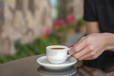 Bir kız kafede kahve içiyor. Kahve dükkanının arka planında, ahşap sehpanın üzerinde beyaz kahve fincanı.