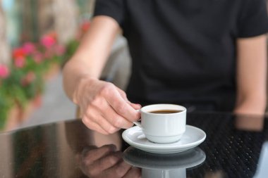 Bir kız kafede kahve içiyor. Kahve dükkanının arka planında, ahşap sehpanın üzerinde beyaz kahve fincanı.