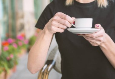 Bir kız kafede kahve içiyor. Kahve dükkanının arka planında, ahşap sehpanın üzerinde beyaz kahve fincanı.