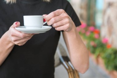 Bir kız kafede kahve içiyor. Kahve dükkanının arka planında, ahşap sehpanın üzerinde beyaz kahve fincanı.