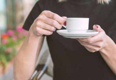 Bir kız kafede kahve içiyor. Kahve dükkanının arka planında, ahşap sehpanın üzerinde beyaz kahve fincanı.