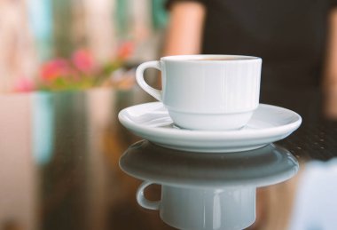 Kahve dükkanının arka planında, ahşap sehpanın üzerinde beyaz kahve fincanı.