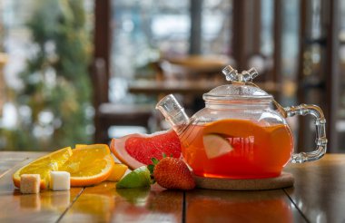 Cam çaydanlıkta meyveli kırmızı çay ve ahşap arka planda fincan.