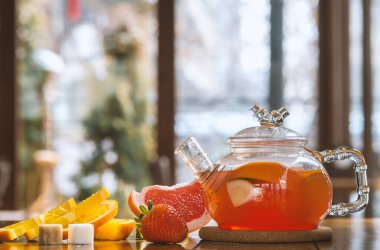 Cam çaydanlıkta meyveli kırmızı çay ve ahşap arka planda fincan.