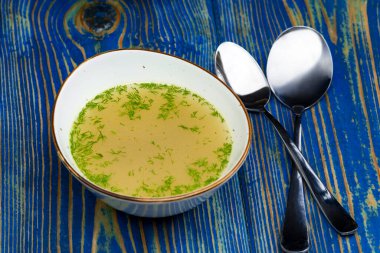 Mavi masadaki beyaz kasede tavuk suyu çorbası.