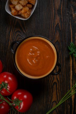 Kahverengi arka planda siyah bir kasede domates çorbası. Üst görünüm.