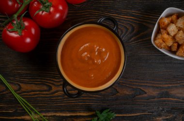 Kahverengi arka planda siyah bir kasede domates çorbası. Üst görünüm.