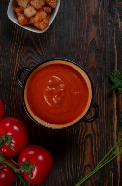 Kahverengi arka planda siyah bir kasede domates çorbası. Üst görünüm.
