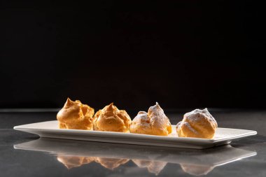 Profiterolleri pudra şekeriyle süslemek. Siyah arkaplanda krema şekerli ekler
