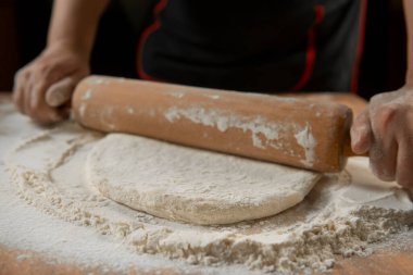 Şef masada merdaneyle hamuru yuvarlıyor. Eller yakın plan. Makarna, ekmek, spagetti, khachapuri, yemek konsepti.